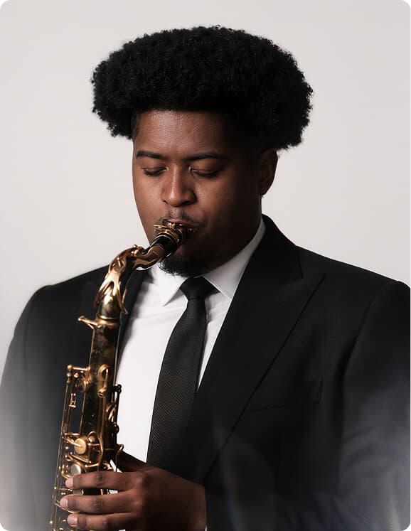 Young saxophonist in a black suit playing against a light background.