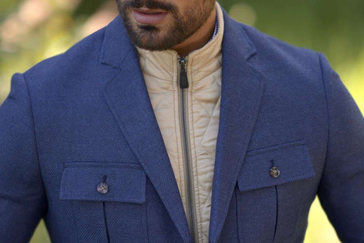 Close-up of a man wearing a blue blazer layered over a quilted cream vest.