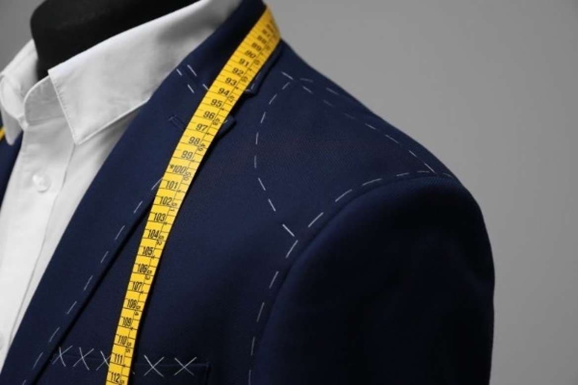 Navy suit jacket with measuring tape and visible tailor stitching.