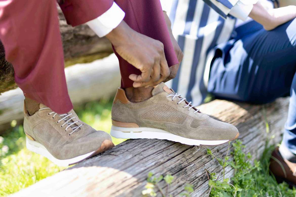 Close-up of beige suede sneakers with burgundy trousers.