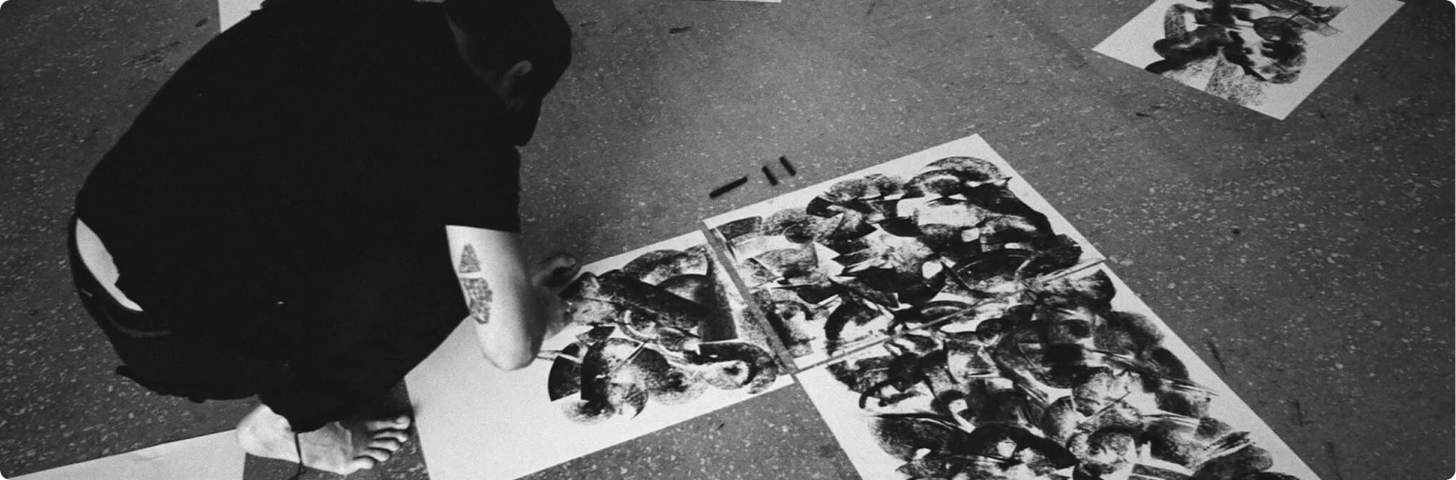 Black-and-white overhead view of an artist working on abstract prints.