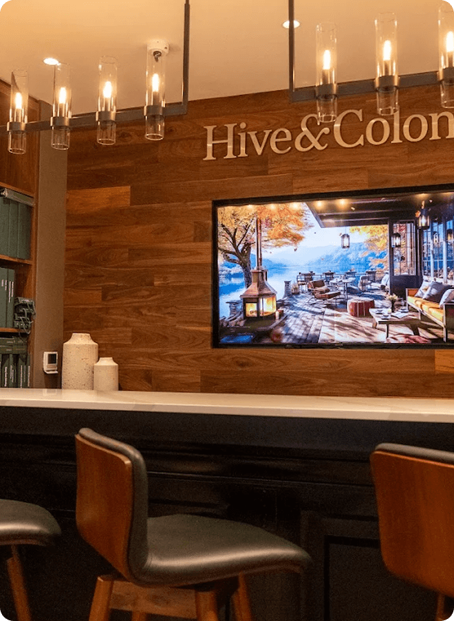Hive & Colony fitting bar with chairs and a screen on a wood wall.