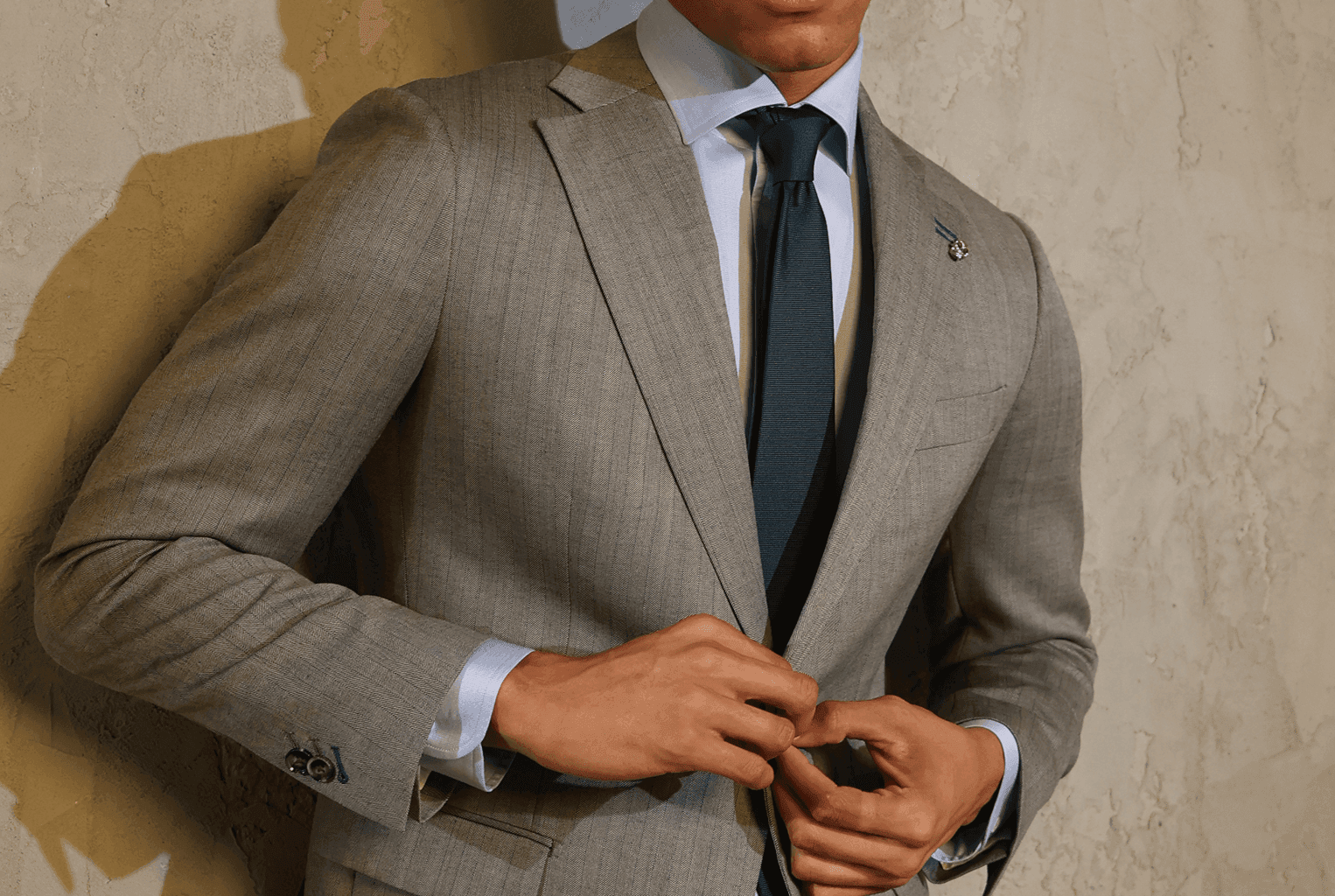 Man fastening a light gray suit jacket with a navy tie.