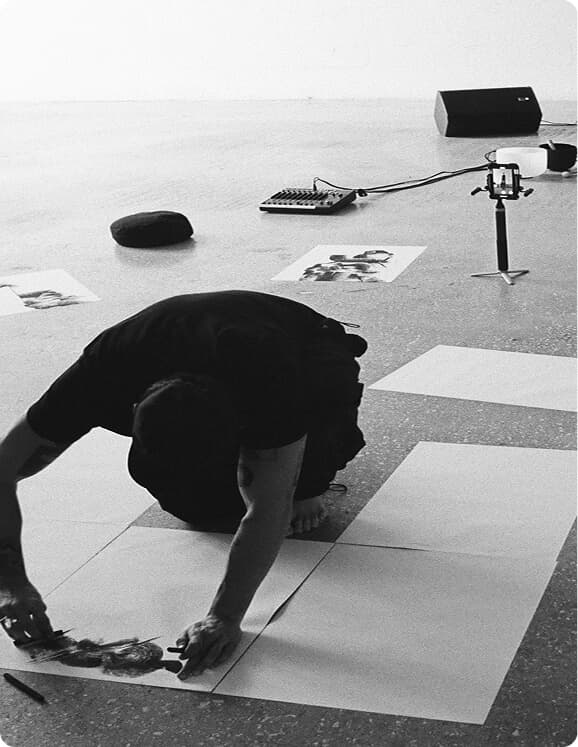 Black-and-white studio scene of an artist working on large papers.