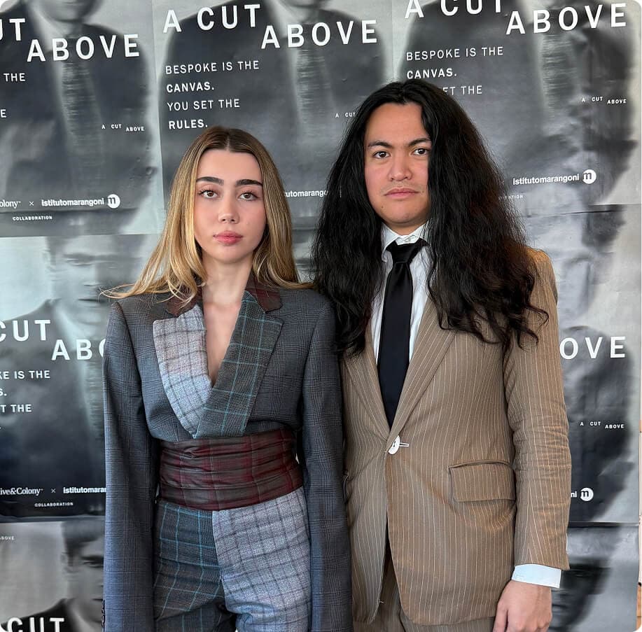 Woman in a gray patchwork suit and man in a tan pinstripe suit posing at the A Cut Above showcase.