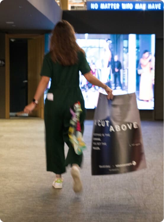 Woman carrying a Cut Above poster through an art gallery.