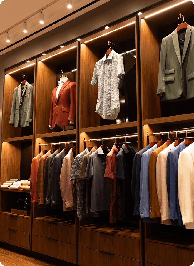 Wooden wardrobe wall displaying jackets, shirts, and tailored garments.