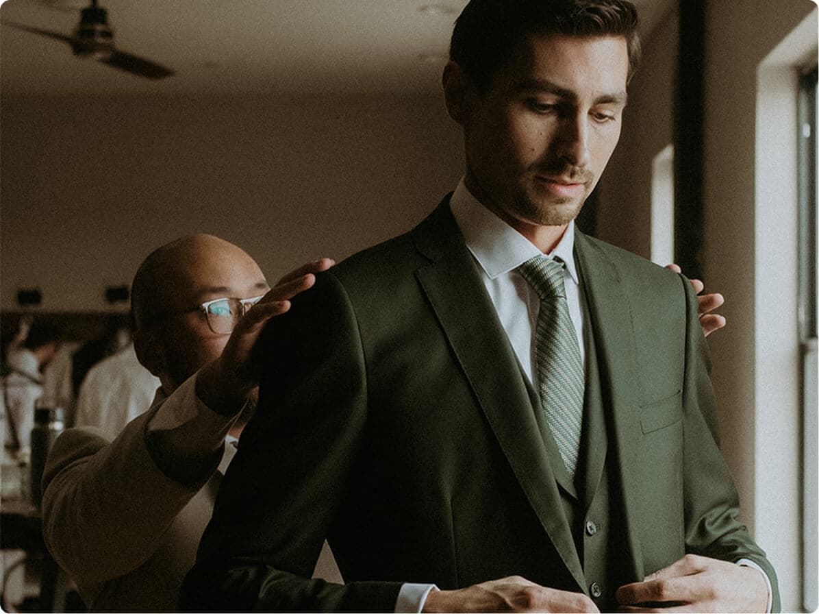Tailor adjusting a man’s green suit jacket.