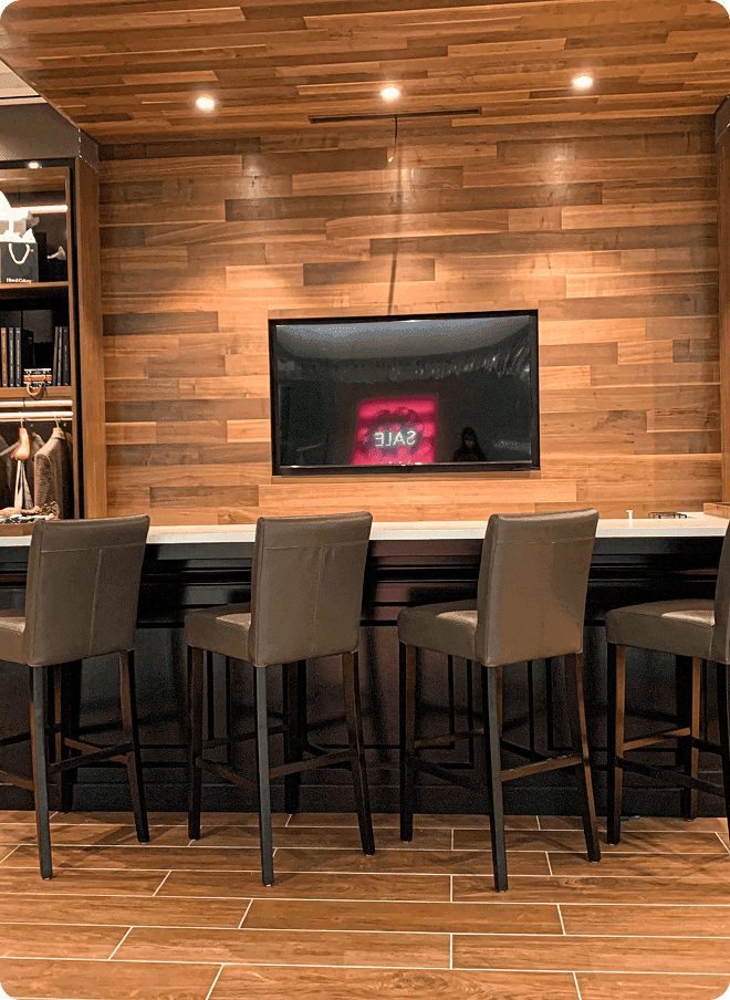 Showroom bar seating in front of a wood wall and wall-mounted screen.