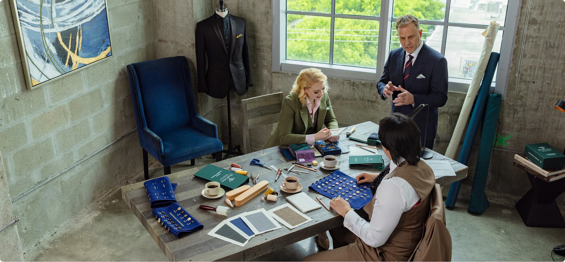 Tailoring team reviewing fabric swatches and buttons at a worktable.