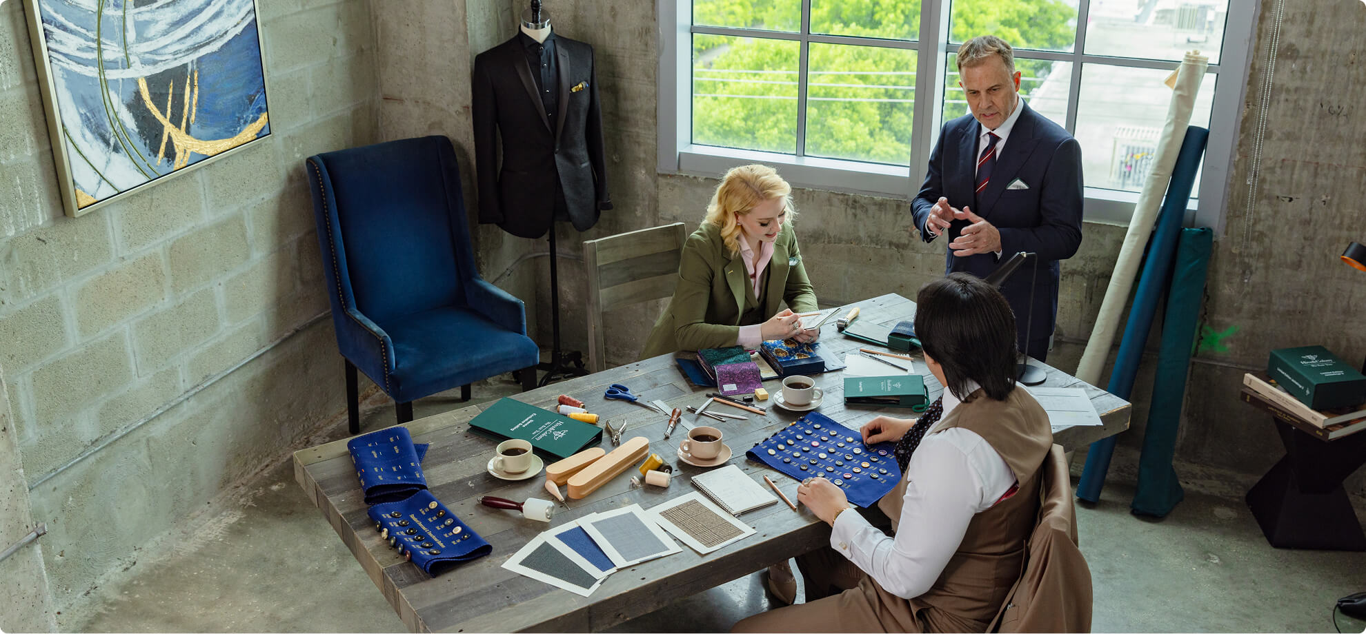 Tailoring team reviewing fabric swatches and buttons at a worktable.