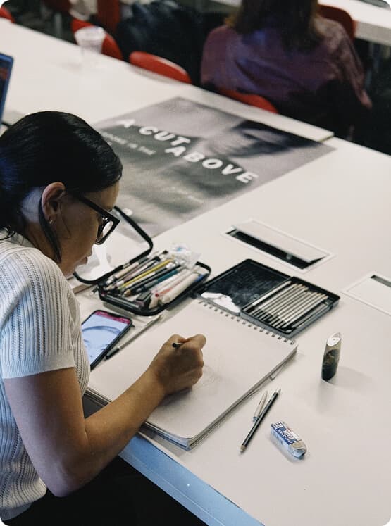 Artist sketching in a notebook at a classroom table.