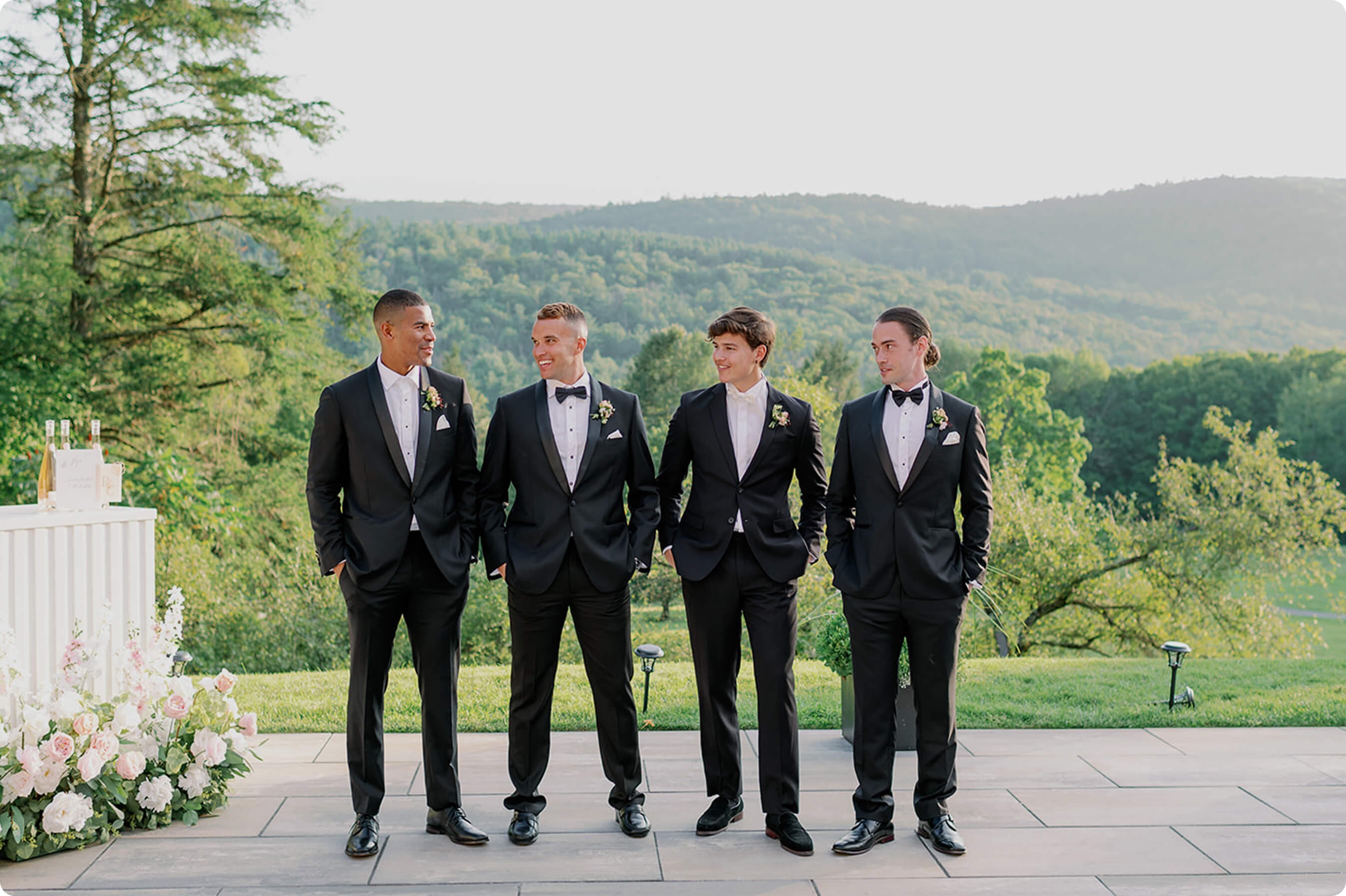 Groomsmen standing outdoors in black tuxedos.