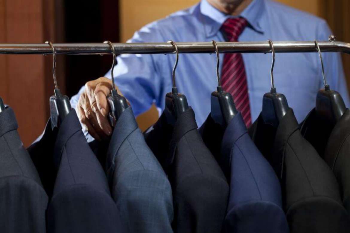 Hand selecting blue and gray suit fabrics from a clothing rack.