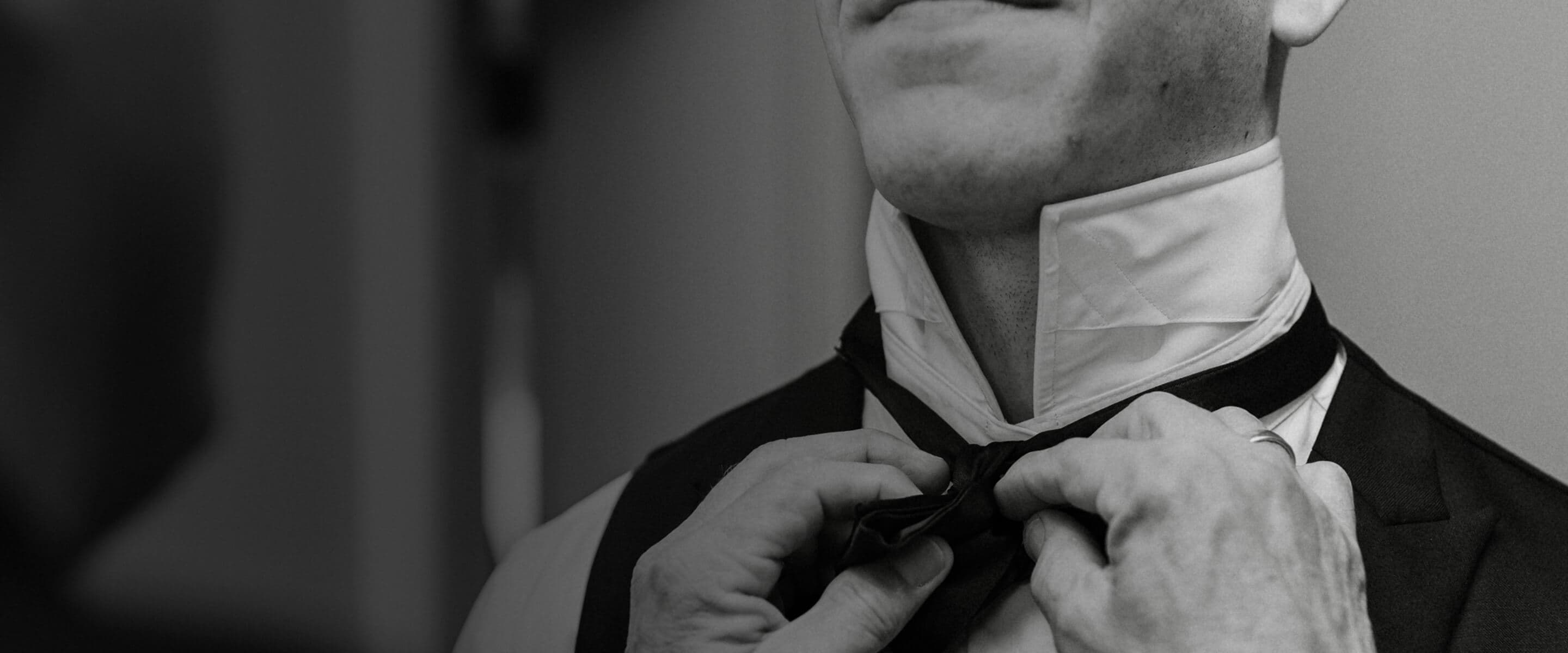 Black-and-white close-up of a groom adjusting his bow tie.