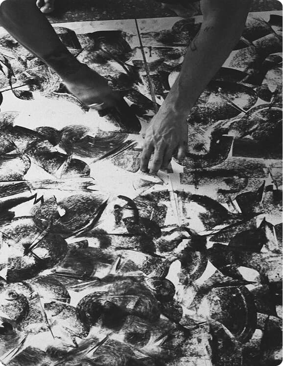 Black-and-white close-up of hands creating abstract artwork.
