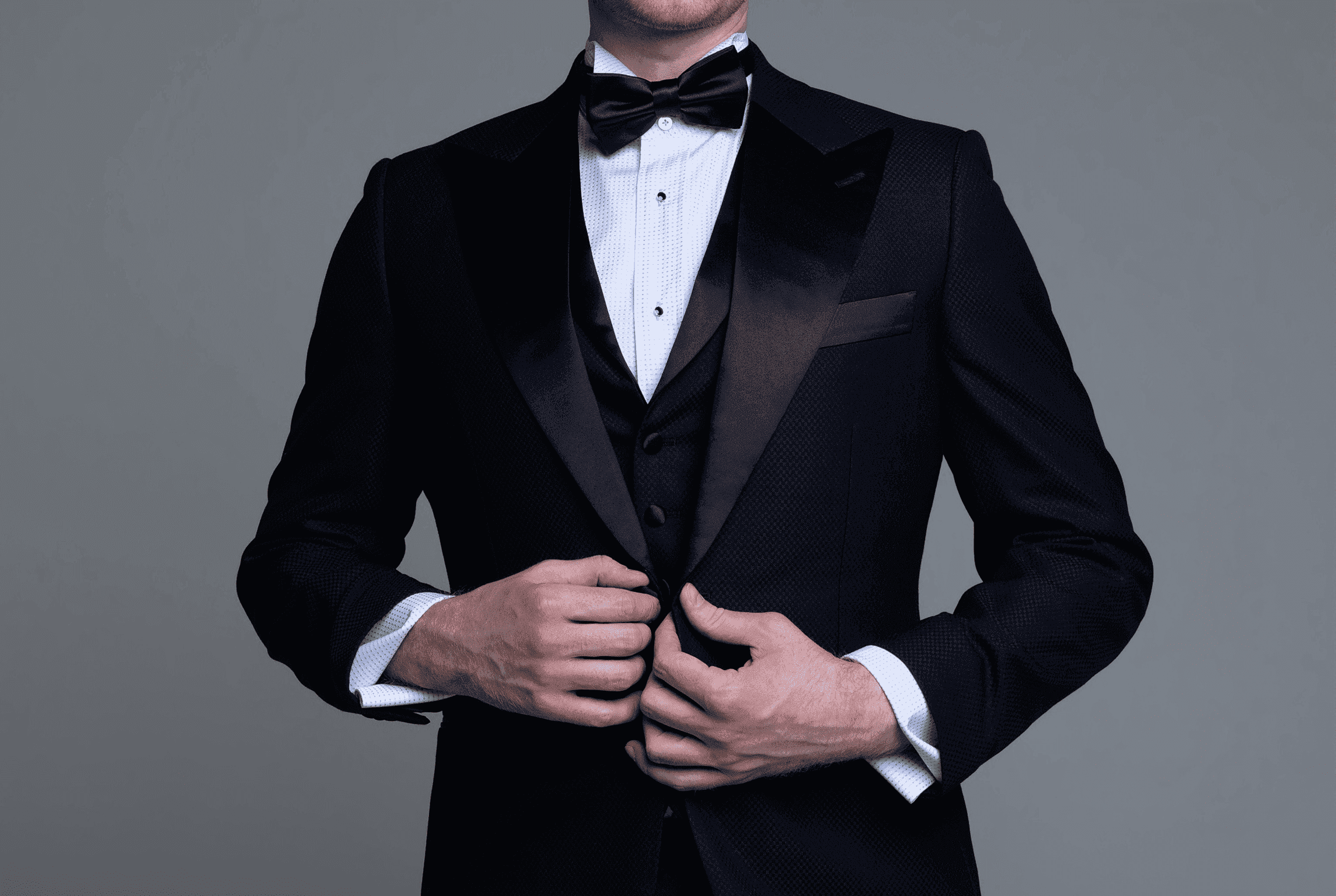 Man in a black tuxedo adjusting the front of his jacket.