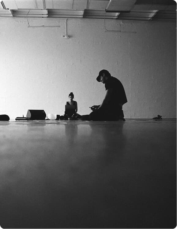 Black-and-white studio scene with two people seated on the floor.