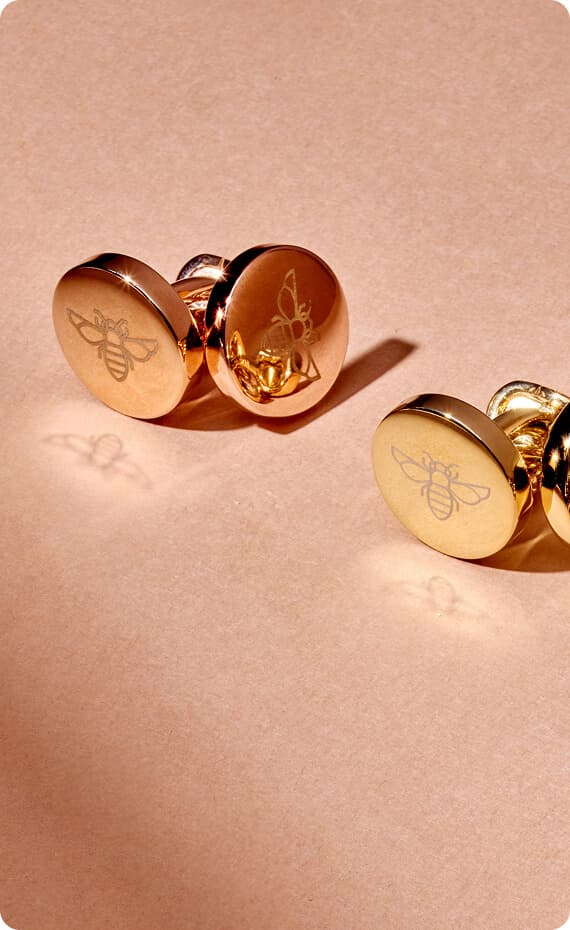 Gold bee cufflinks arranged on a warm textured surface.