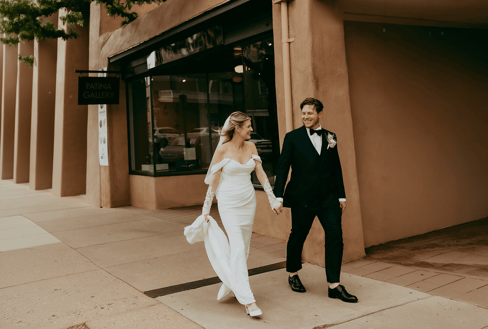 Bride and groom holding hands while walking down a street