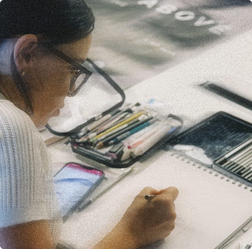 Fashion student sketching a garment beside colored pencils and drawing tools.