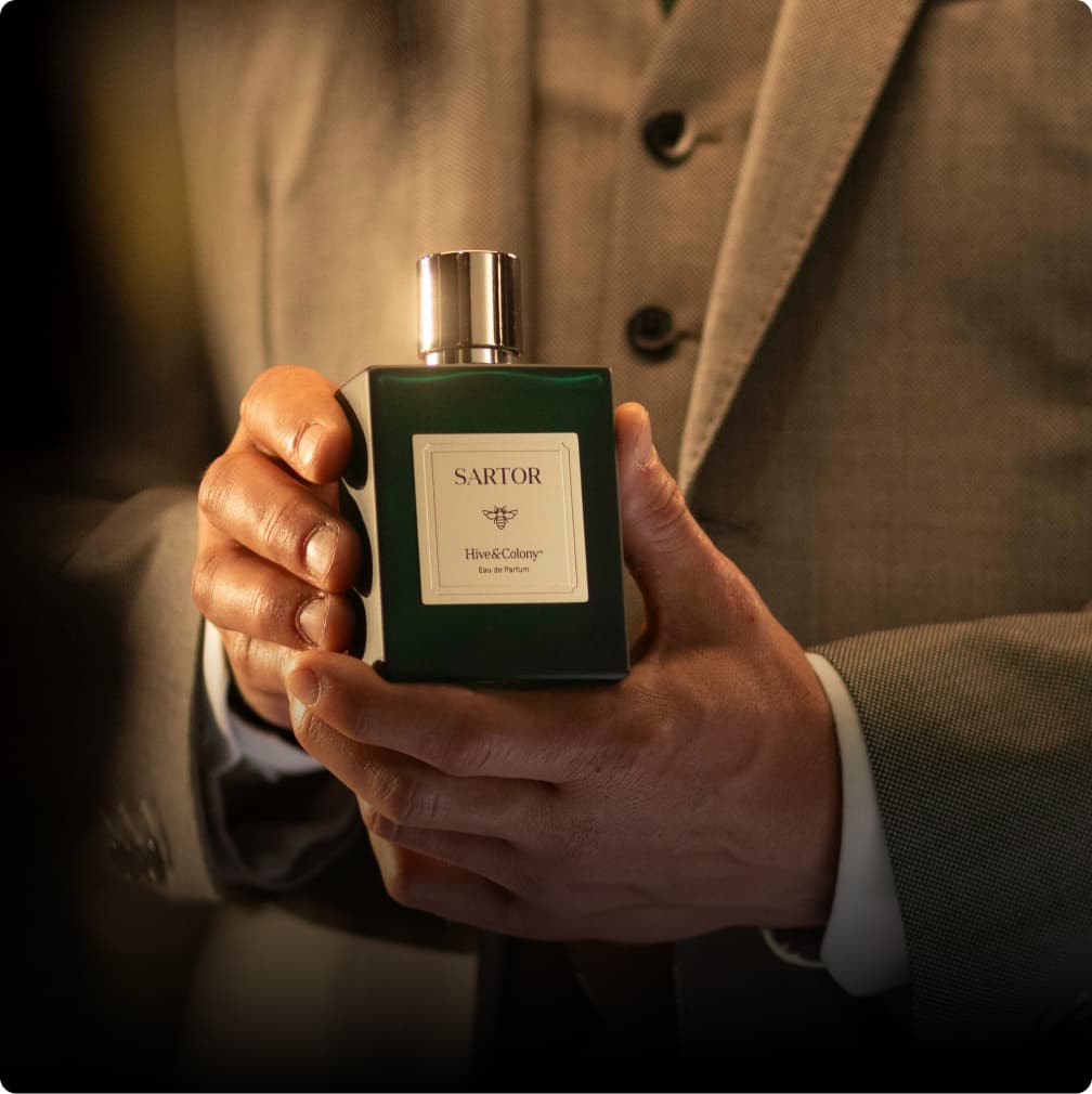Hand holding a green Sartor fragrance bottle in warm lighting.