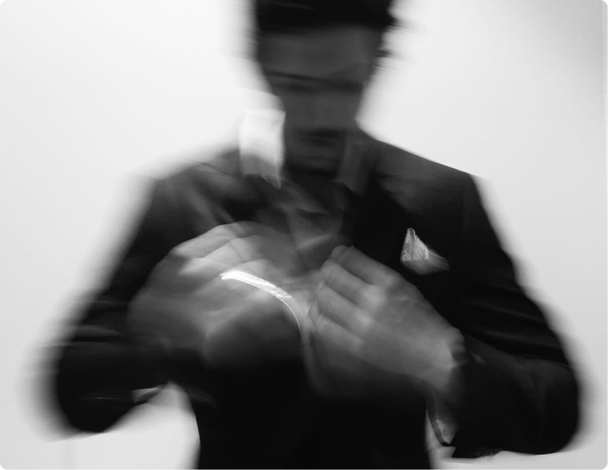 Blurred black-and-white image of a man adjusting a suit jacket.