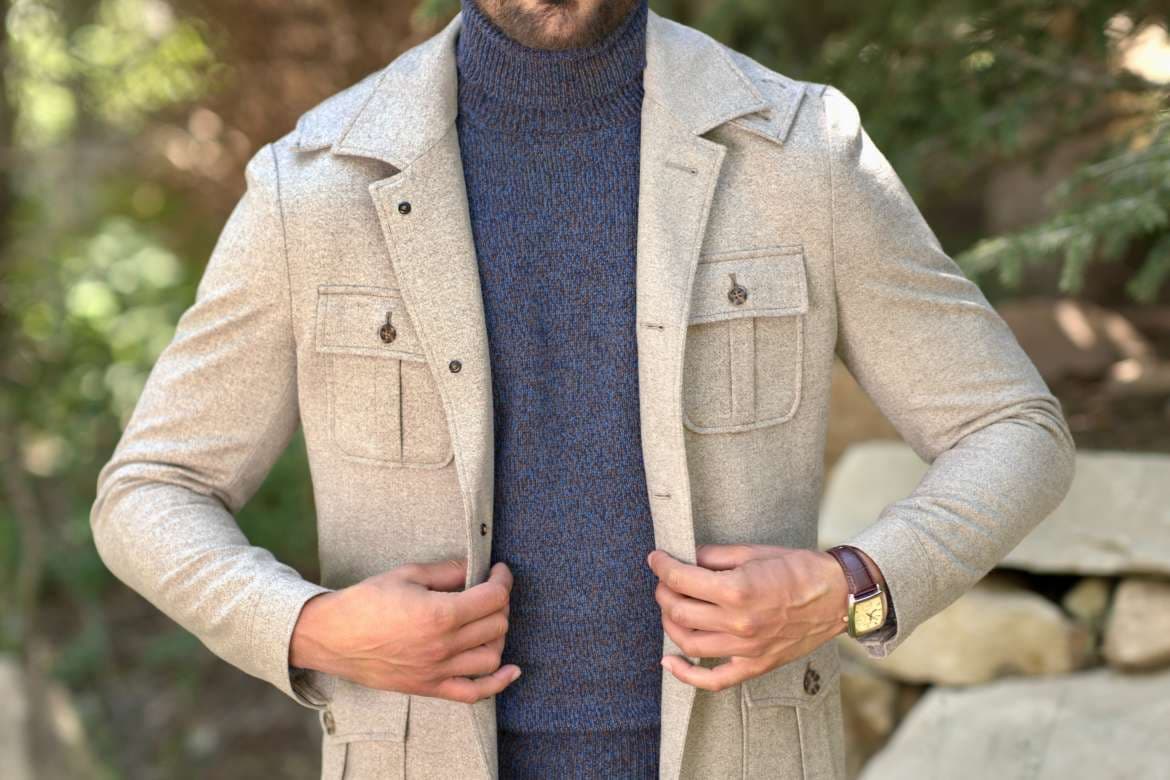 Close-up of a man adjusting a beige field jacket over a blue turtleneck outdoors.